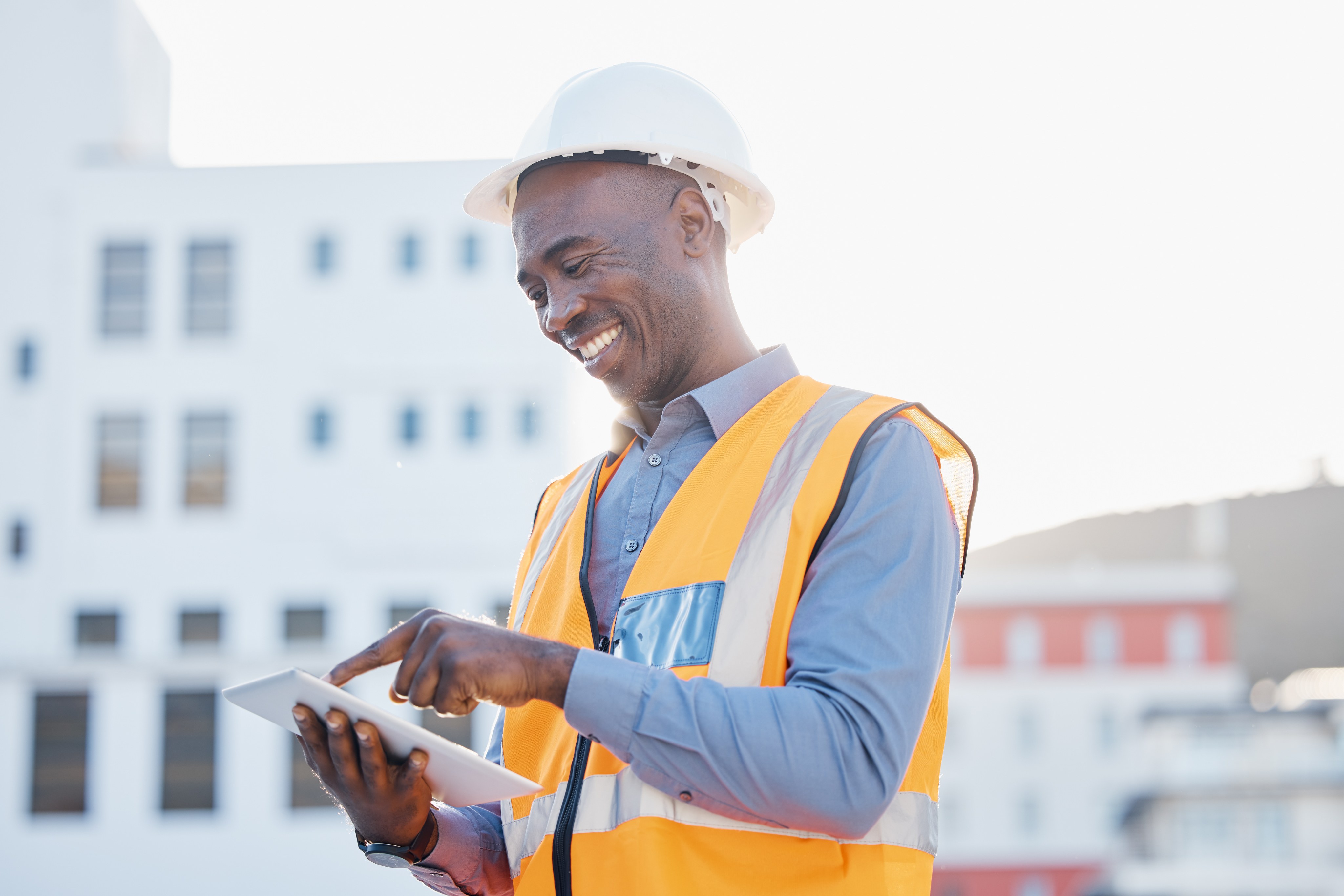 Smiling project manager in safety vest holding tablet on construction site